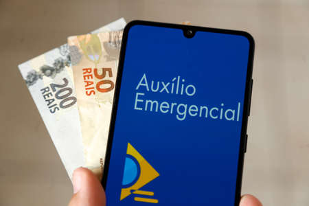 Minas Gerais, Brazil - April 6, 2021: Emergency Aid in mobile phone application and money bills