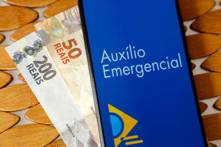 Minas Gerais, Brazil - April 6, 2021: Emergency Aid in mobile phone application and money billsのeditorial素材