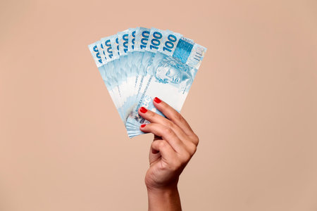 several hundred real bills - money from Brazil in a womans hand with red nails