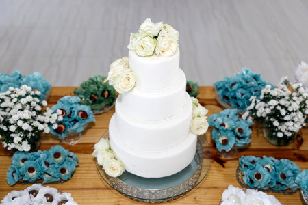 white birthday cake with four parts, with white flowers and various sweets on the tableの写真素材