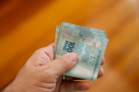 Sharp image of hand holding one hundred Brazilian real bills, perfect for finance, economy, investment, and wealth themes in Brazilの写真素材