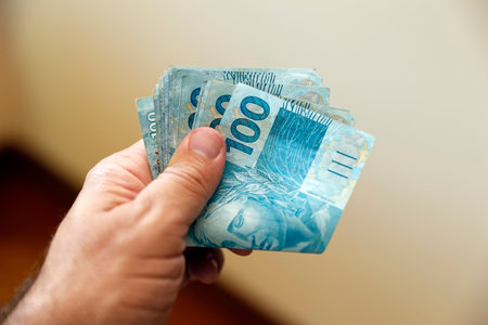 Close-up of hand holding multiple one hundred Brazilian real bills, perfect for finance, wealth,...