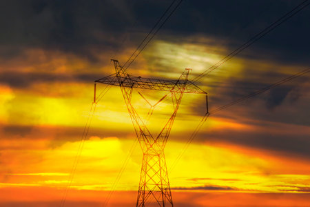 Electric power transmission tower in open field, with wires connecting infrastructure to nature,...