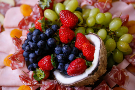 Gourmet charcuterie with cured meats, fresh strawberries, grapes in half coconut shell. Creative...