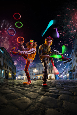 Night street circus performance whit two clowns, juggler. Festival city background. fireworks and Celebration atmosphere.の写真素材