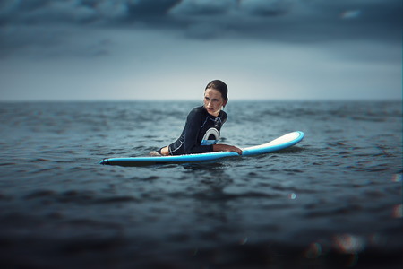 girl with surf board wait big ocean wave,dramatic sky and toning. lifestyle, people water sport lessons and beach swimming activity on summer vacationの写真素材