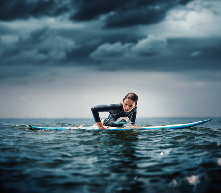 girl with surf board wait big ocean wave,dramatic sky and toning. lifestyle, people water sport lessons and beach swimming activity on summer vacationの写真素材