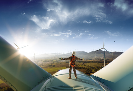 Happy engineer feel success after good work. He standing a top of windmill and looking beautiful sunset landscapeの写真素材