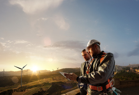 Windmill engineer and businessman planing new ecology project. they standing and looking in tablet. Around wind generators and beautiful landscapeの写真素材