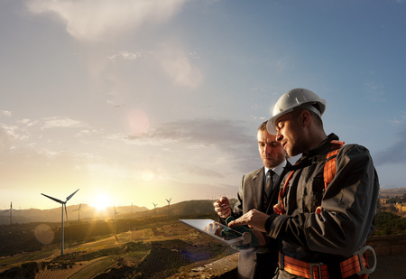 Windmill engineer and businessman planing new ecology project. they standing and looking in tablet. Around wind generators and beautiful landscapeの写真素材