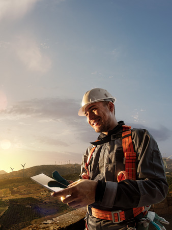 Happy engineer planning new project. He standing a top mount and looking in tablet. around beautiful landscapeの写真素材