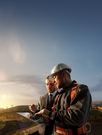Windmill engineer and businessman planing new ecology project. they standing and looking in tablet. Around wind generators and beautiful landscapeの写真素材