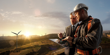 Windmill engineer and businessman planing new ecology project. they standing and looking in tablet. Around wind generators and beautiful landscapeの写真素材