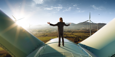 Happy businessman feel success after good work. He standing a top of windmill and looking beautiful sunset landscapeの写真素材