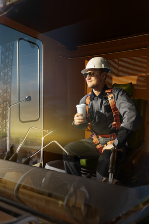 Happy engineer feel success after good work. He sit a top of crane cabin drink coffee and looking beautiful sunsetの写真素材