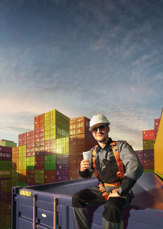Happy Engineer sit in stack containers. His happy drinking coffee after successful work. Photo with...