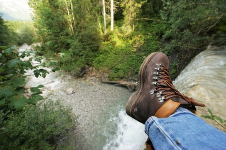 Young man resting at a waterfall, you can see the mountain bootsの写真素材