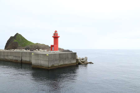 A red lighthouse at a pier near an oceanの写真素材