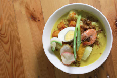 Green curry with prawns and egg in white bowl on wooden tableの写真素材