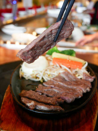 Beef sirloin being grilled on black plate with chopsticksの写真素材