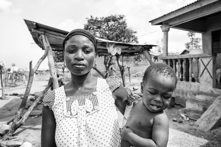 PORTO-NOVO, BENIN - MAR 8, 2012: Unidentified Beninese mother carries her little child in her hands People of Benin suffer of poverty due to the difficult economic situation.のeditorial素材