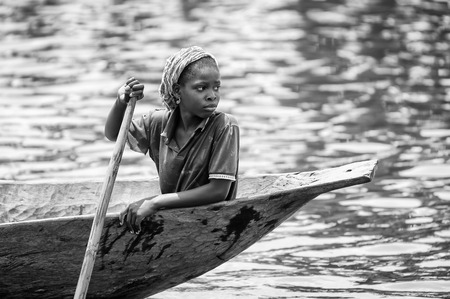 PORTO-NOVO, BENIN - MAR 9, 2012: Unidentified Beninese woman rows a wooden boat. People of Benin suffer of poverty due to the difficult economic situation.のeditorial素材