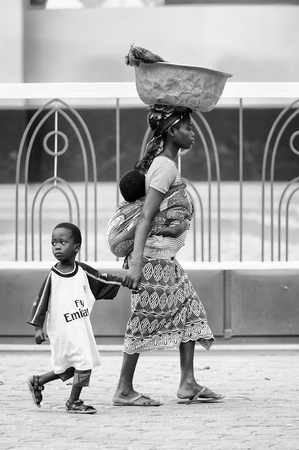 PORTO-NOVO, BENIN - MAR 10, 2012: Unidentified Beninese woman a son and a little child on a back. People of Benin suffer of poverty due to the difficult economic situationのeditorial素材