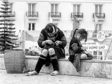 SAPA, VIETMAN - SEP 22, 2014: Unidentified Hmong woman and her daughter are sewing in the street in Sapa, Vietnam. Hmong is a minority ethnic group of Vietnamのeditorial素材