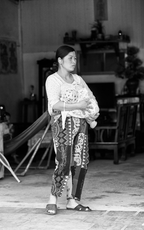 SAPA, VIETMAN - SEP 22, 2014: Unidentified Hmong woman with her baby on arms drinking brest milk in Sapa, Vietnam. Hmong is a minority ethnic group of Vietnamのeditorial素材