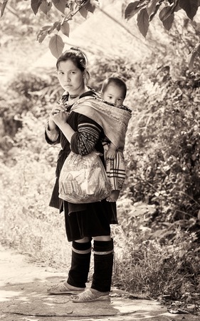 LAO CHAI, VIETMAN - SEP 22, 2014: Unidentified Black Hmong women with her little baby on her back in Lao Chai, Vietnam. Hmong is a ethnic minority group in Vietnamのeditorial素材