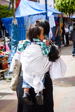 OTAVALO, ECUADOR - JAN 3, 2015: Unidentified Ecuadorian woman carries her little baby at the Otavalo Market. 71,9% of Ecuadorian people belong to the Mestizo ethnic groupのeditorial素材