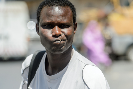 SAINT LOUIS, SENEGAL - APR 24, 2017: Unidentified Senegalese man in white shirt holds a wooden stick in his mouth in the centre of Saint Louis, one of the major cities in Senegalのeditorial素材