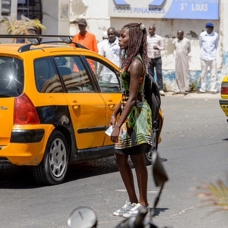 SAINT LOUIS, SENEGAL - APR 24, 2017: Unidentified Senegalese woman with braids holds a backpack and walks along the road in the centre of Saint Louis, one of the major cities in Senegalのeditorial素材
