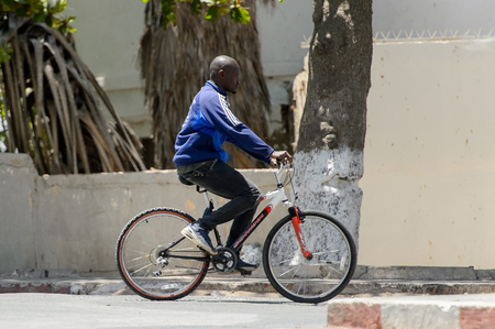 SAINT LOUIS, SENEGAL - APR 24, 2017: Unidentified Senegalese man rides a bicycle in the centre of Saint Louis, one of the major cities in Senegalのeditorial素材