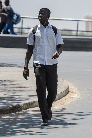 SAINT LOUIS, SENEGAL - APR 24, 2017: Unidentified Senegalese man in white shirt with backpack walks along the road in the centre of Saint Louis, one of the major cities in Senegalのeditorial素材