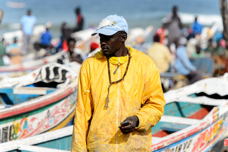 KAYAR, SENEGAL - APR 27, 2017: Unidentified Senegalese man in yellow shirt walks on the coast of the Atlantic Ocean. Many Kayar people work in portのeditorial素材