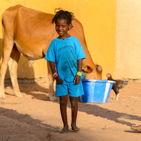 FERLO DESERT, SENEGAL - APR 25, 2017: Unidentified Fulani little girl in blue suit plays on the street. Fulanis (Peul) are the largest tribe in West African savannahsのeditorial素材