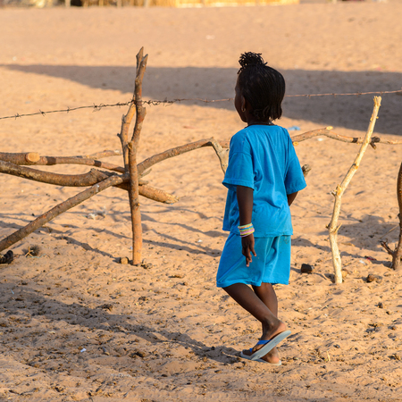 FERLO DESERT, SENEGAL - APR 25, 2017: Unidentified Fulani little girl in blue suit plays on the street. Fulanis (Peul) are the largest tribe in West African savannahsのeditorial素材