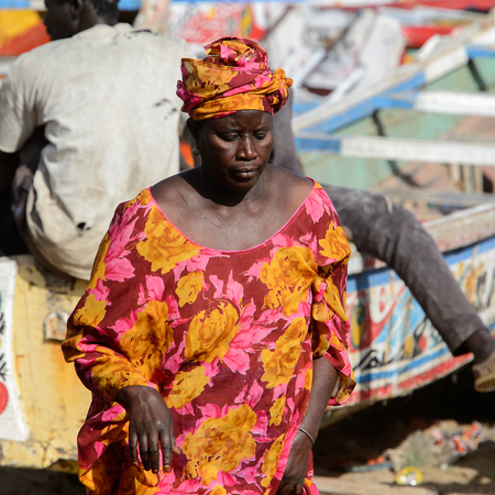 KAYAR, SENEGAL - APR 27, 2017: Unidentified Senegalese woman in traditional clothes walks on the coast of the Atlantic Ocean. Many Kayar people work in portのeditorial素材