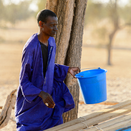 FERLO DESERT, SENEGAL - APR 25, 2017: Unidentified Fulani man in violet clothes walks along the...
