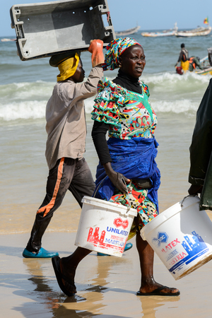 KAYAR, SENEGAL - APR 27, 2017: Unidentified Senegalese man carries a box on his head on the coast of the Atlantic Ocean. Many Kayar people work in portのeditorial素材