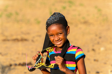 FERLO DESERT, SENEGAL - APR 25, 2017: Unidentified Fulani little girl in striped shirt and black headscarf smiles. Fulanis (Peul) are the largest tribe in West African savannahsのeditorial素材