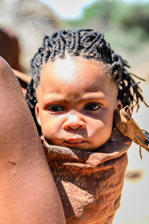 EAST OF WINDHOEK, NAMIBIA - JAN 3, 2016: Unidentified bushman baby on his mother back. Bushman...