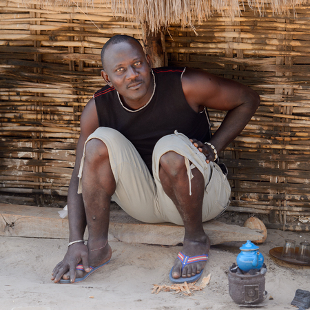 KASCHOUANE, SENEGAL - APR 29, 2017: Unidentified Diola man sits on the ground near the fence in...