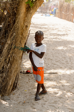 KASCHOUANE, SENEGAL - APR 29, 2017: Unidentified Diola little boy stands near the tree trunk in Kaschouane village. Diolas are the ethnic group predominate in the region of Casamanceのeditorial素材