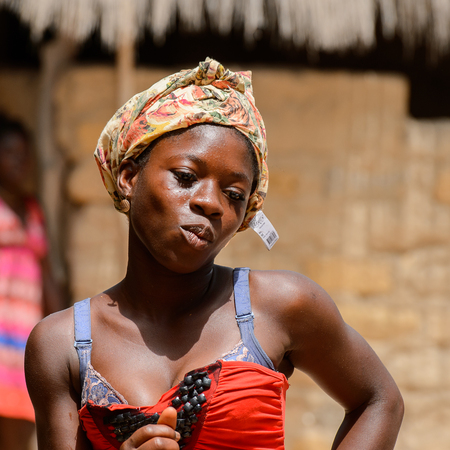 ORANGO ISLAND, GUINEA BISSAU - MAY 3, 2017: Unidentified local woman in red dress and headscarf looks down in the Etigoca village. People in G.-Bissau still suffer of povertyのeditorial素材