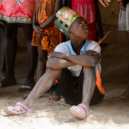 ORANGO ISLAND, GUINEA BISSAU - MAY 3, 2017: Unidentified local little boy in a hat made of paper sits on the ground in the Etigoca village. People in G.-Bissau still suffer of povertyのeditorial素材