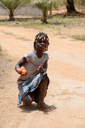 CANCHUNGO, GUINEA BISSAU - MAY 3, 2017: Unidentified local little girl with braids collects vegetables for lunch. Bissau-Guinean people suffer of poverty due to the bad economyのeditorial素材