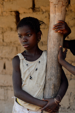 CANHABAQUE, GUINEA BISSAU - MAY 4, 2017: Unidentified local little girl with braids stands near the wooden pole in a village of the Canhabaque island. People in G.-Bissau still suffer of povertyのeditorial素材