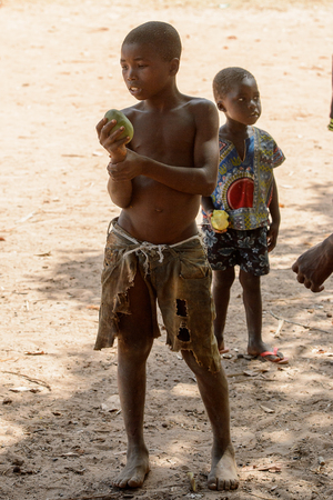 CANHABAQUE, GUINEA BISSAU - MAY 4, 2017: Unidentified local boy in shorts holds a fruit in a village of the Canhabaque island. People in G.-Bissau still suffer of povertyのeditorial素材